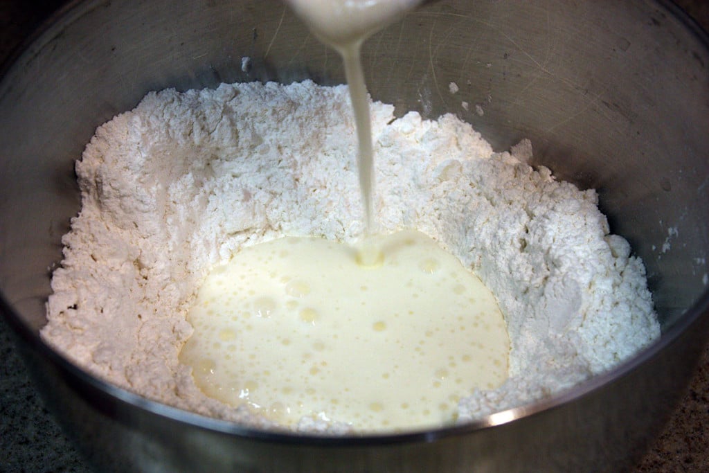 Buttermilk being poured into the center of the flour.