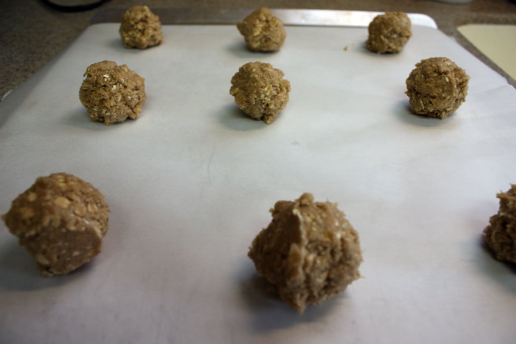 Oatmeal cookie dough balls on a parchment paper lined baking sheet.
