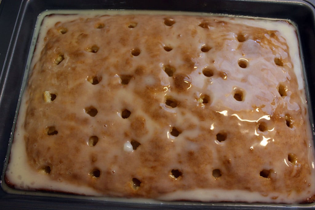 Coconut sheet cake with holes poked into it with the coconut cream mixture poured over.
