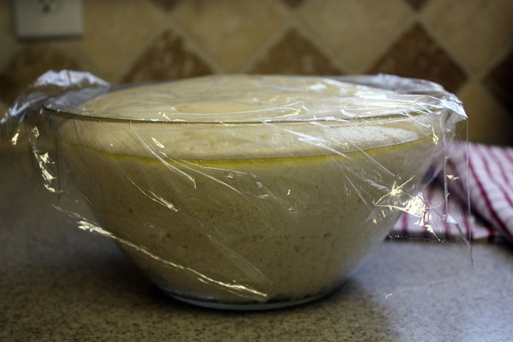 Risen naan dough in a glass bowl.
