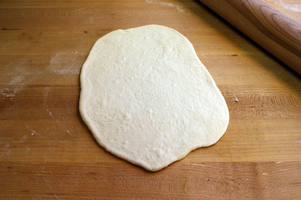 Dough ball rolled out flat on a wooden board.