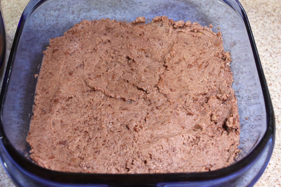 Refried black beans spread into a square pan.