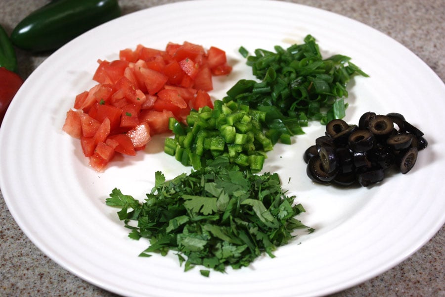 Diced tomatoes, jalapenos, green onions, black olives, and cilantro on a plate.