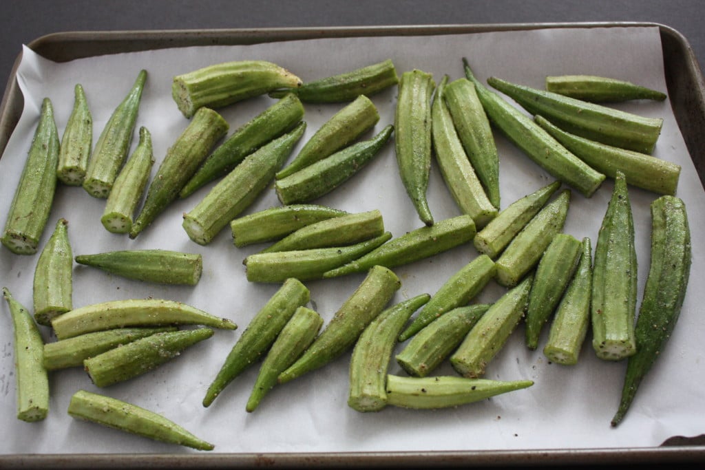 Okra pods on a parchment paper lined baking sheet.