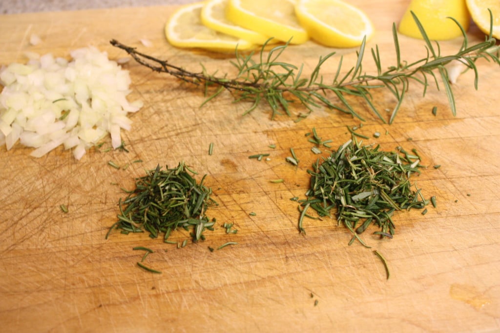 Chopped onions, rosemary, and lemons on a wooden board.