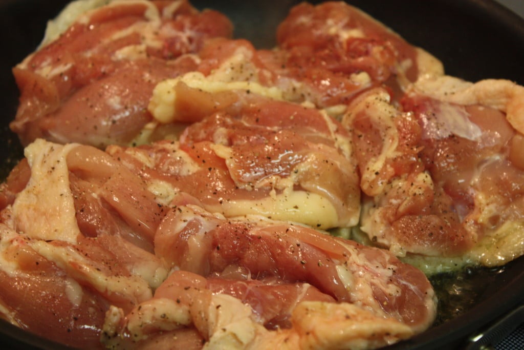 Chicken thighs skin-side down browning in a skillet.