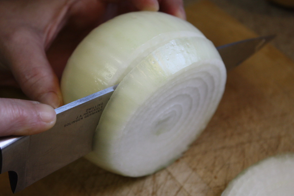 Onion being sliced on a wooden board.