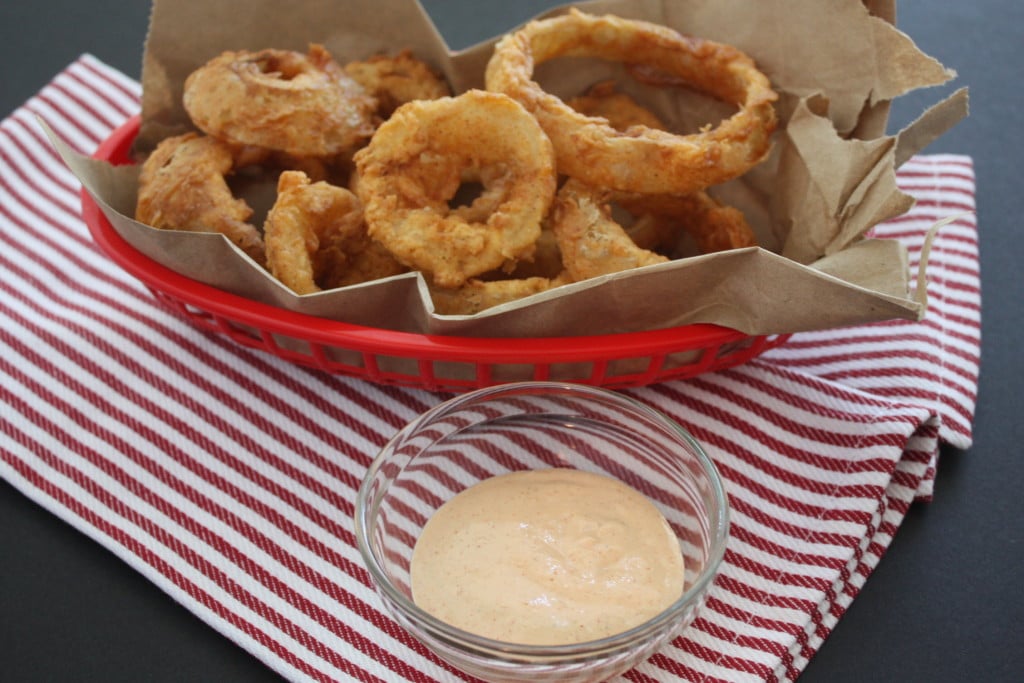 Buttermilk battered onion rings in a brown paper lined red basket.