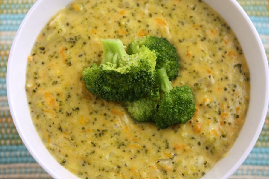 Broccoli Cheese Soup in a white bowl garnished with broccoli florets.