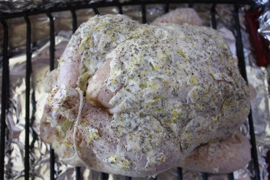 Whole chicken rubbed with the compound butter on a rack in a roasting pan.