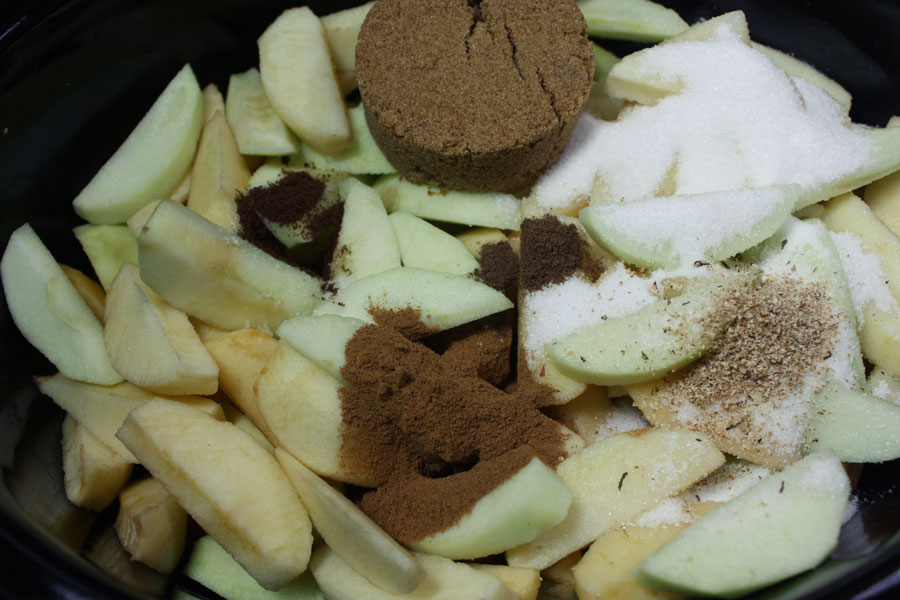 Peeled and slice apples topped with spices in a slow cooker crock.