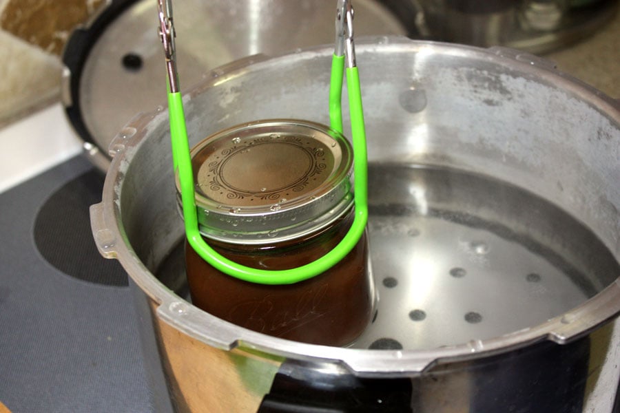 apple butter in a mason jar being placed into a pressure cooker