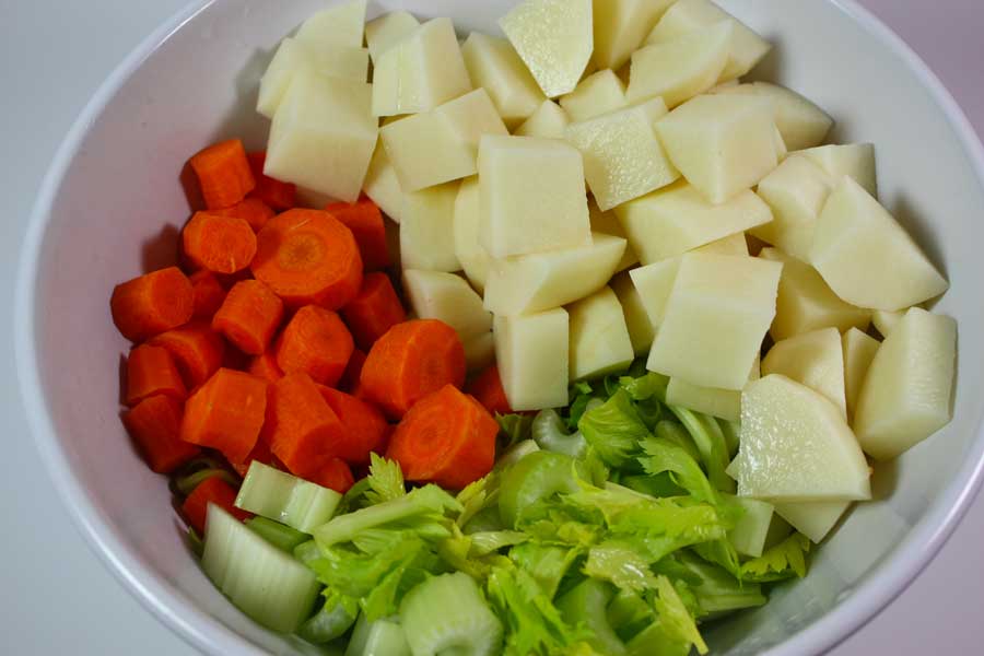 Diced potatoes, carrots, and celery in a white bowl.