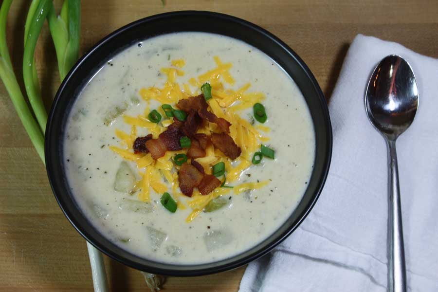 Creamy Potato Soup in a black bowl garnished with cheese, bacon crumbles, and diced green onions