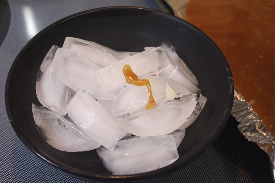 Candy dripped onto ice cubes in a black bowl.