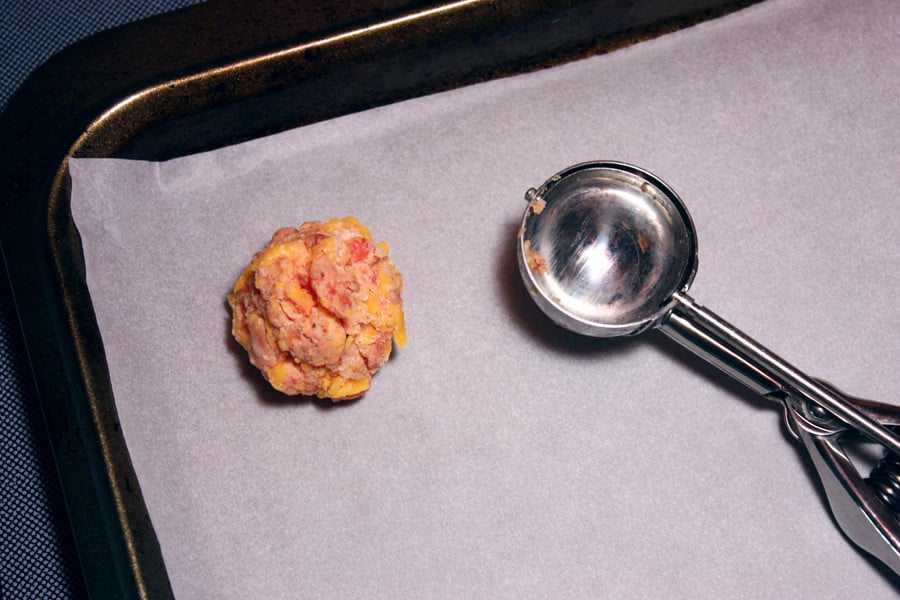 One sausage ball formed on a parchment lined baking sheet.