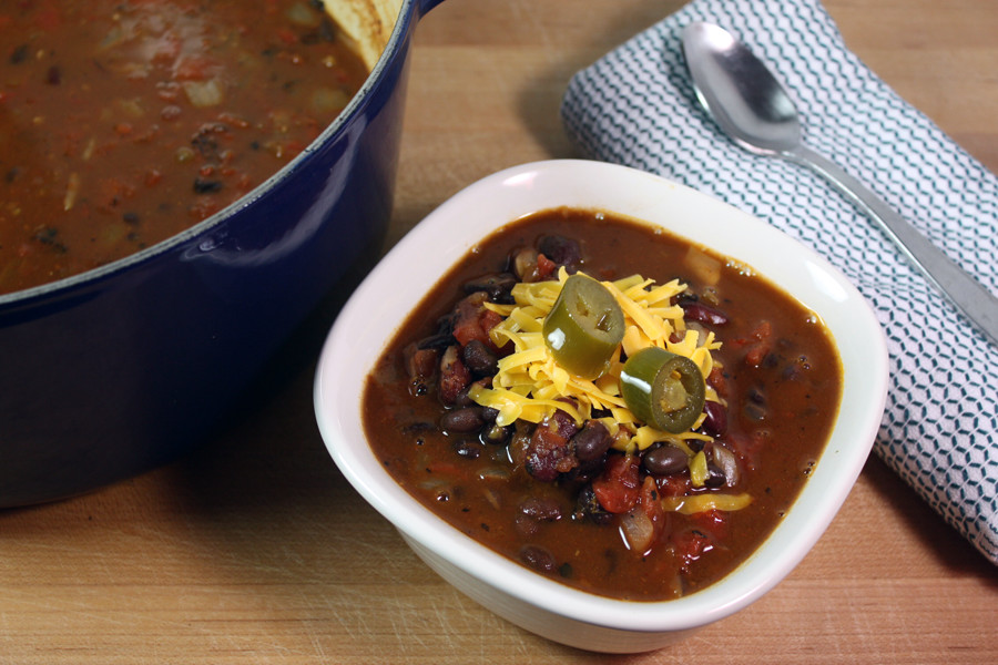 Vegetarian Chili in a white bowl garnished with shredded cheese and jalapeno slices.