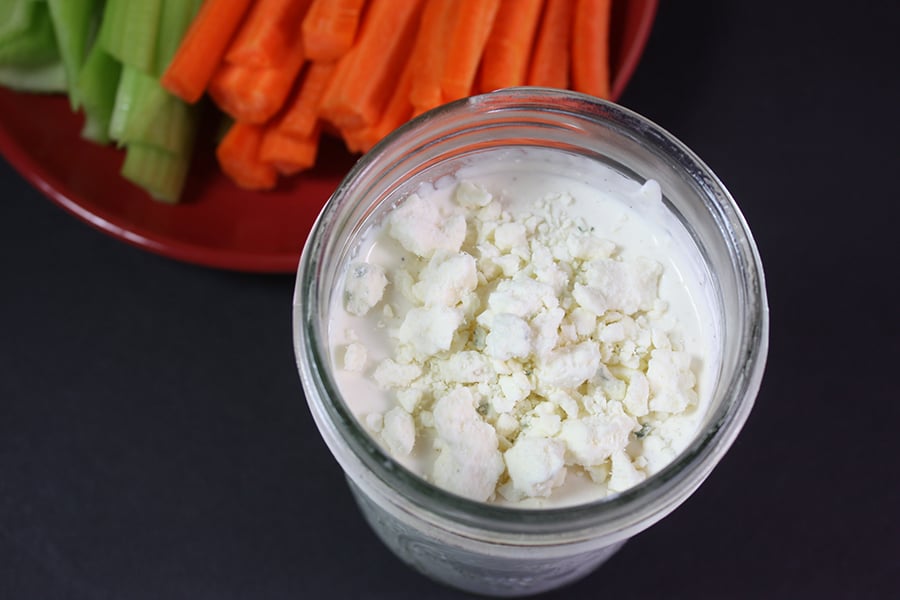 Blue Cheese Dressing in a mason jar with carrot sticks and celery sticks on a plate in the background.