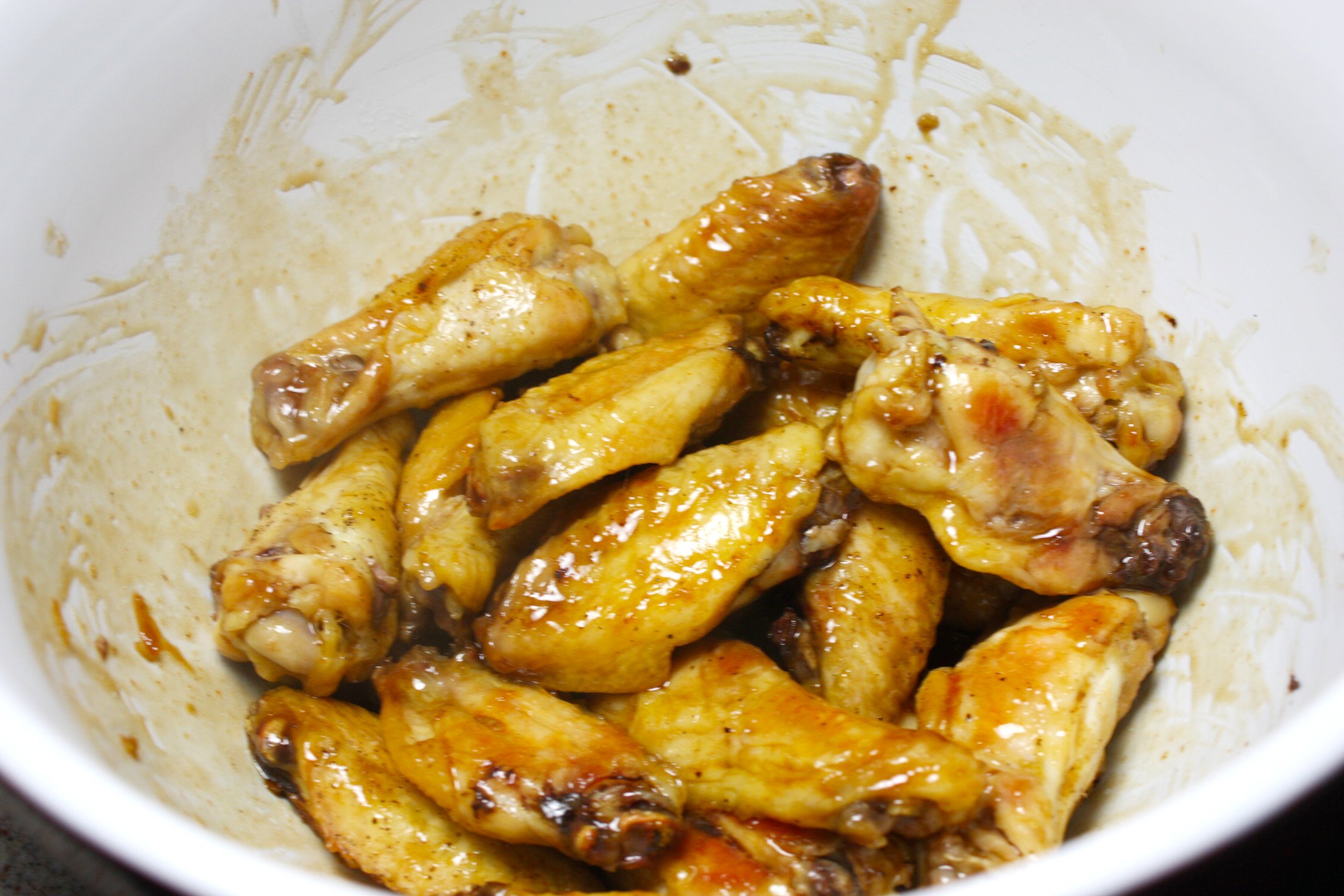 Cooked chicken wings tossed with the sauce in a white bowl.