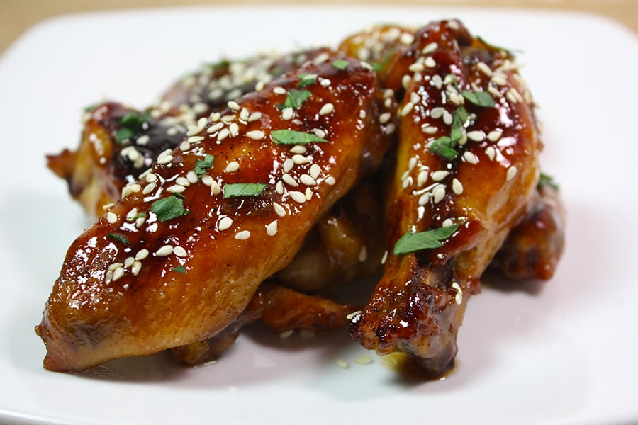 Honey Sriracha Chicken Wings garnished with sesame seeds and chopped parsley on a white plate.