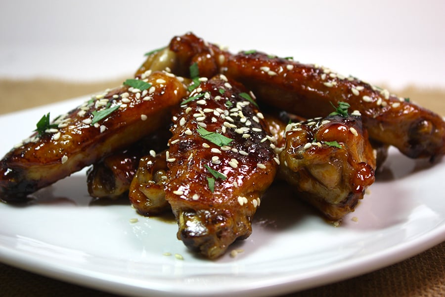 Honey Sriracha Wings on a white plate and a sesame garnish.