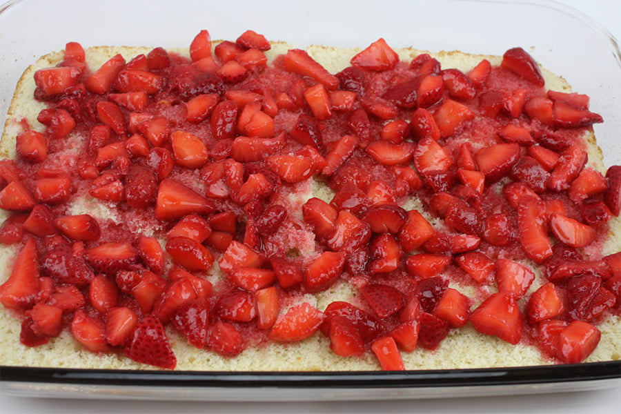 Bottom half of the shortcake topped with cut strawberries and syrup.