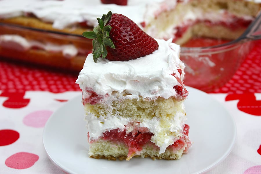 A slice of Strawberry Shortcake on a white plate garnished with a strawberry on top.