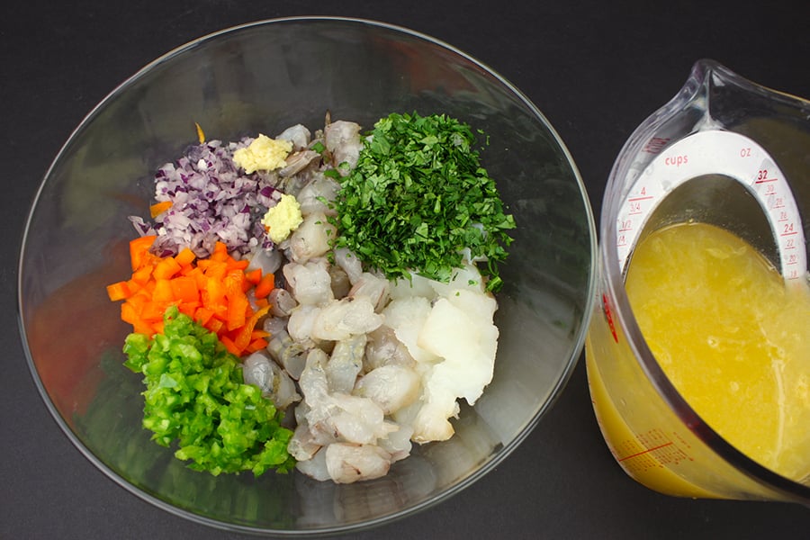 Ingredients for shrimp and cod ceviche in a glass bowl next to the marinade ingredients in a measuring cup.