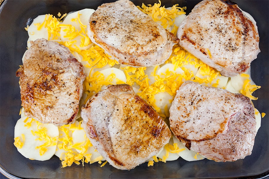 Smothered Pork Chops and Potatoes - sliced potatoes, shredded cheese, and pork chops in a baking dish