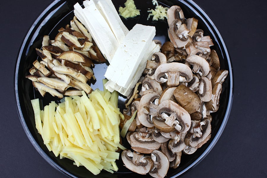 Mushrooms, bamboo shoots, tofu, garlic, ginger on black plate.