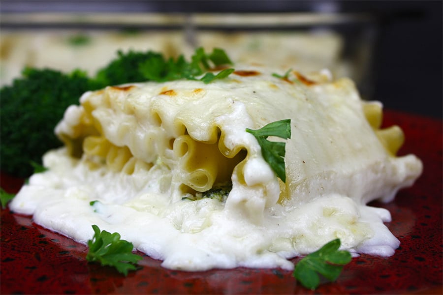 Broccoli Alfredo Lasagna Roll-Ups on a red plate garnished with chopped parsley