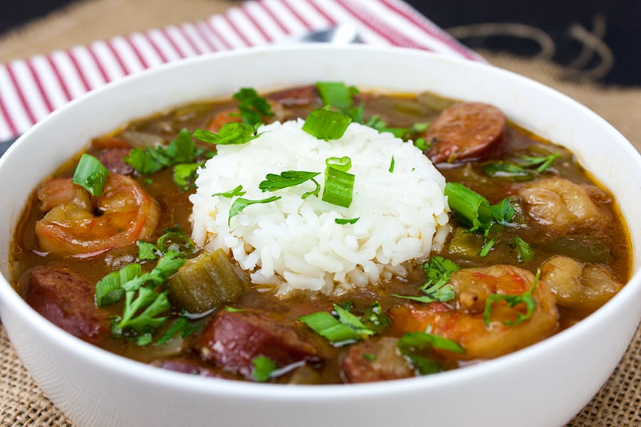 Shrimp and Sausage Gumbo in a white bowl with rice added to the middle and garnished with green onions and parsley.