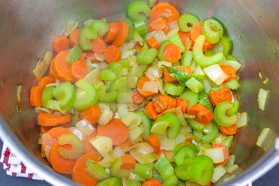 Celery, carrots, and onions sautéed in a pan.