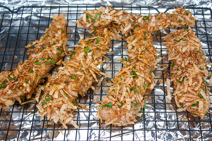 Unbaked parmesan crusted chicken tenders on a wire rack over a foil-lined baking sheet.