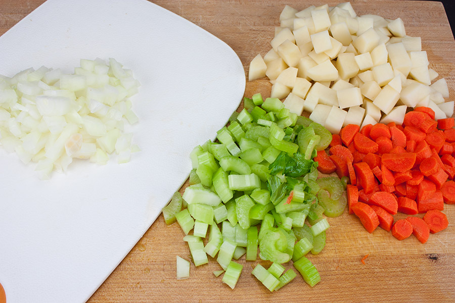 Diced carrots, celery, onions, and potatoes on a wooden cutting board.