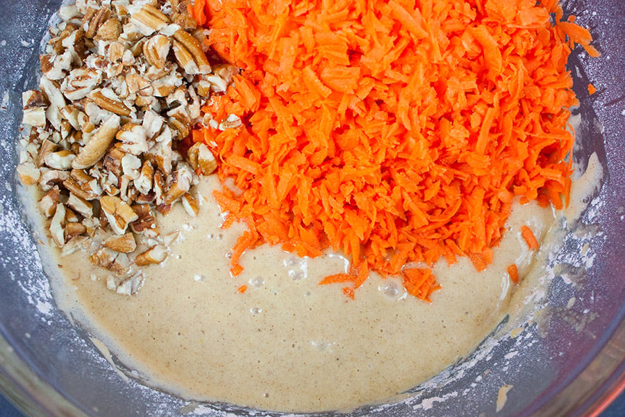 Carrot cake batter in mixing bowl with grated carrots and chopped pecans added.