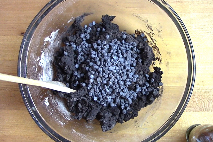 Dark chocolate biscotti dough topped with chocolate chips in a glass mixing bowl.
