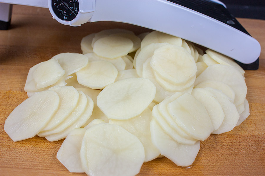 Creamy Herb Potatoes Gratin - potatoes sliced thin on a wooden cutting board