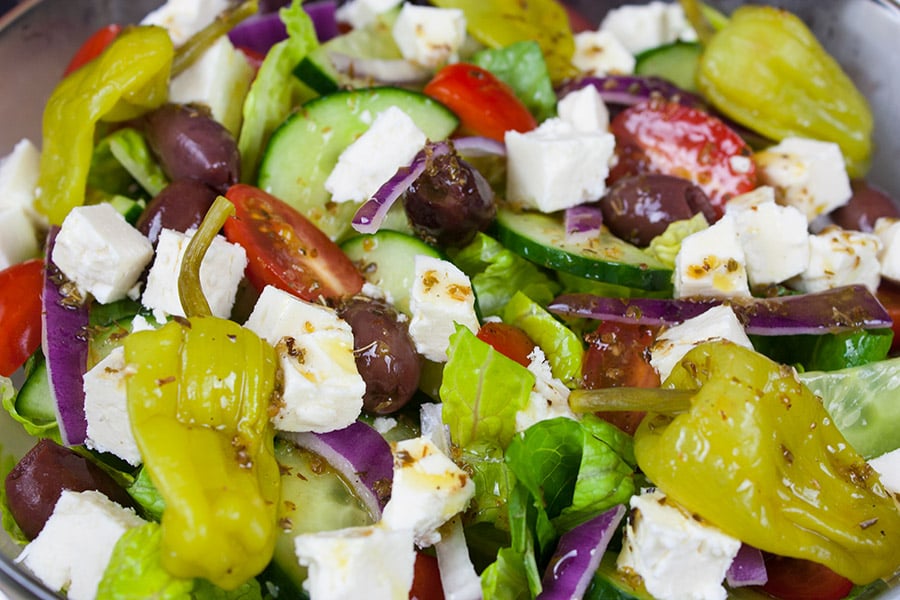 Dressed Greek salad in a chilled glass bowl.
