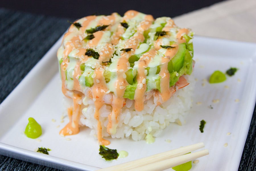 Spicy Shrimp Sushi Stack drizzled with sauces on a square white plate with chopsticks