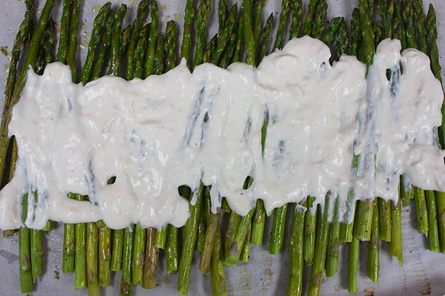 Roasted Asparagus on a baking sheet with horseradish sour cream sauce spread over the middle