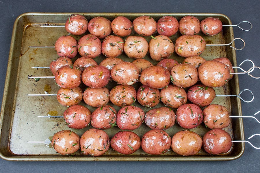 Skewered parboiled marinated baby red potatoes on a baking sheet.