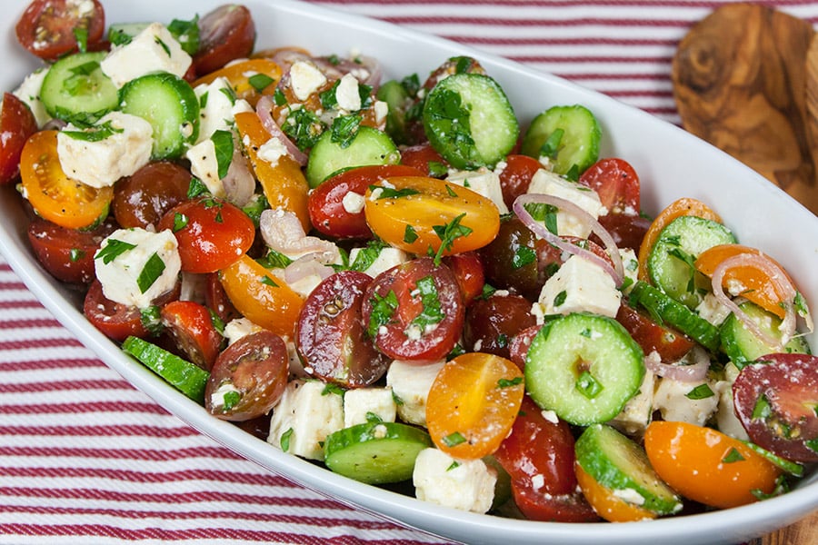 Tomato Cucumber Feta Salad in a white serving bowl on a red and white striped cloth