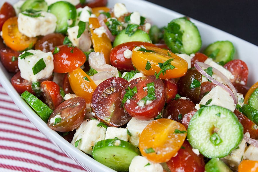 Tomato Cucumber Feta Salad in a white serving bowl on a red and white stripe cloth