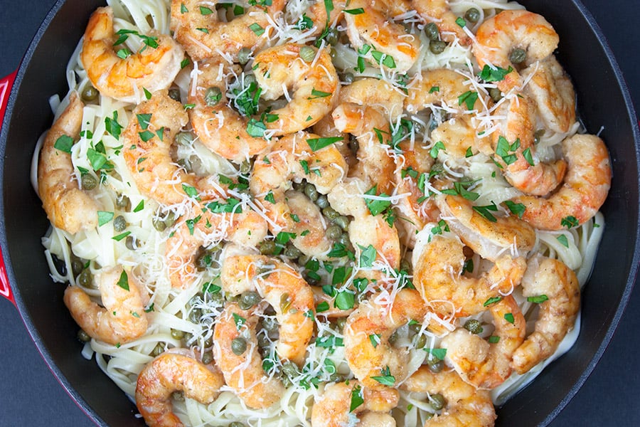 Shrimp Piccata in red cast iron skillet garnished with Parmesan cheese and fresh parsley