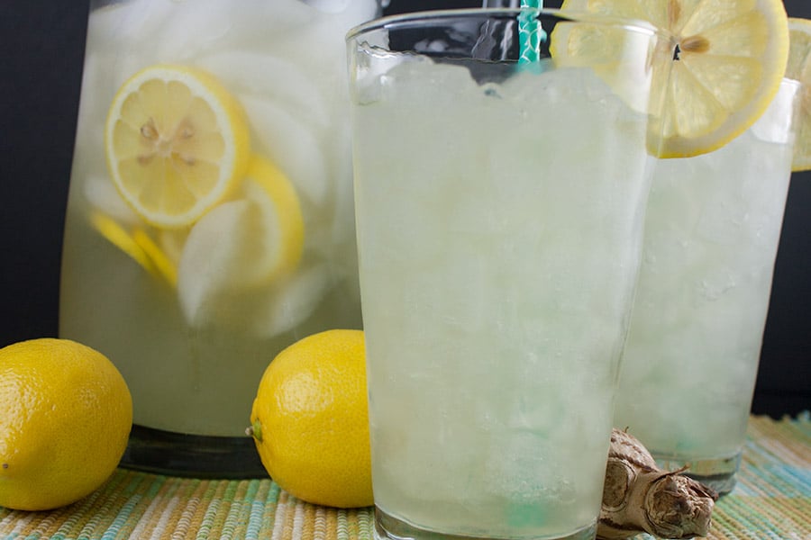 Honey Ginger Lemonade in glass pitcher and two tall glasses garnished with lemon slices