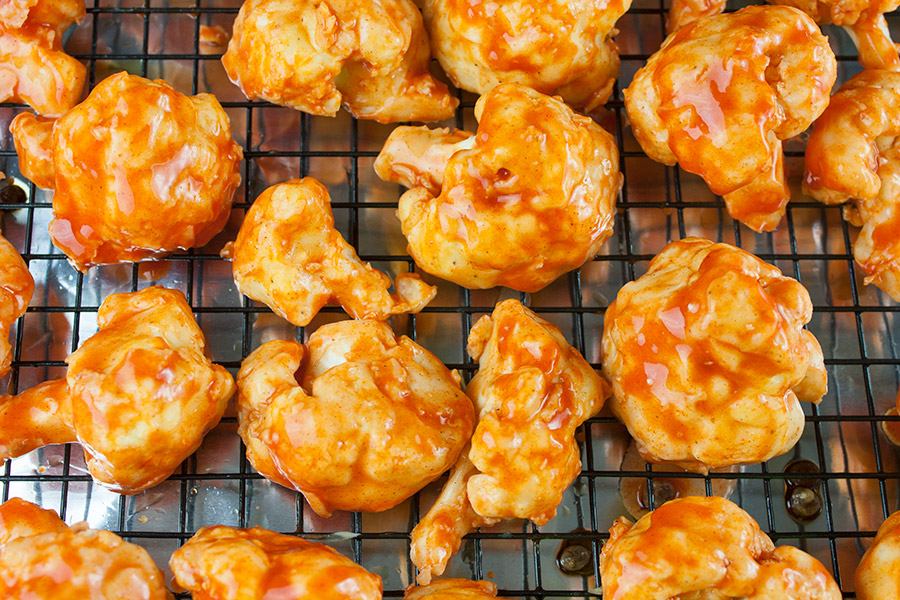 Cauliflower bites tossed with buffalo sauce on a wire rack.