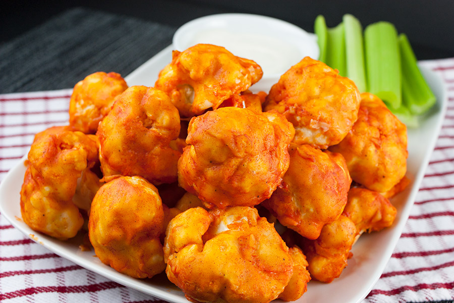 Baked Buffalo Cauliflower Bites in a white serving bowl with celery sticks on the side.