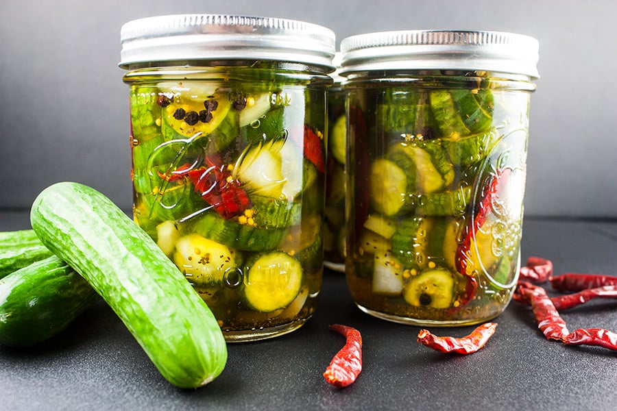 Spicy Bread and Butter Pickles in canning jars fresh pickles and dried peppers scattered around.