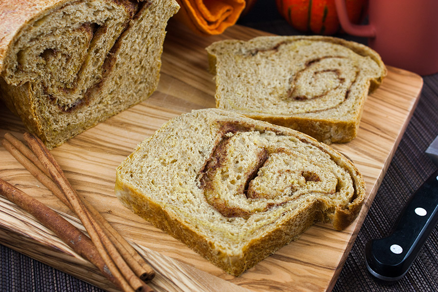 Pumpkin Cinnamon Swirl Bread loaf sliced on a wooden cutting board